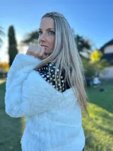 Chaqueta corta de piel sintética blanca con interior de gamuza negra y apliques de tachas plateadas y doradas en la espalda.