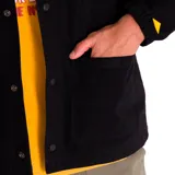 Chaqueta tipo coach de color negro, confeccionada en tejido twill de algodón. Presenta cierre frontal con botones a presión, cuello clásico, puños elásticos y múltiples bolsillos frontales, incluyendo bolsillos en el pecho y en la parte inferior. Incluye etiqueta con logo de la marca en el pecho.