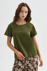 Remera de algodón verde militar, de manga corta y corte holgado, con cuello redondo a la base y detalle de cinta perforada en los hombros.