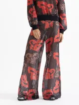Pantalón Lexi de punto calado con estampado full print en tonos rojos, negros y marrones. Tiene cintura elastizada y bota amplia.