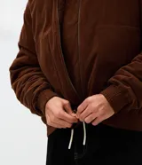 Campera bomber de pana color marrón, con cuello polo, cierre frontal con cremallera y puños y bajo elásticos.