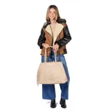 Cartera tipo tote de gran tamaño en color taupe, confeccionada en símil cuero con textura granulada. Presenta doble asa larga para llevar al hombro, cierre de cordones laterales y placa metálica frontal con logo grabado.
