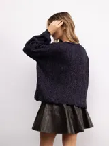 Sweater de punto oversize en color bordó con destellos de lurex. Presenta un diseño acanalado vertical, cuello redondo y mangas largas con terminaciones acampanadas y bordes ondulados.