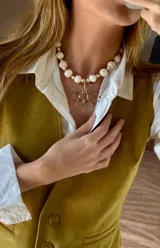 Collar de piedras blancas irregulares y cuentas doradas, con dije colgante de bronce en forma de sol estilizado.