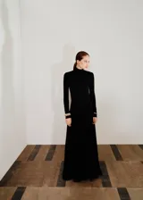 Vestido largo de fiesta color negro, con cuello alto, manga larga y diseño evasé. Presenta un corte en pico en la cintura y forro interior.