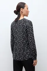 Blusa negra con estampado de lunares blancos, escote en V y mangas largas con puños abotonados.
