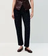 Pantalón de jean corte mom, color azul oscuro, con cintura alta y detalle de remaches metálicos distribuidos por toda la prenda. Cuenta con cierre frontal, botón y bolsillos funcionales.