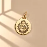 Dije circular de oro 18K con el grabado del Escudo Nacional de Uruguay en el centro y argolla superior para cadena.