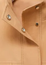 Chaqueta oversize de lyocell color beige, con cuello alto, cierre frontal oculto con botones y cremallera, bolsillos de solapa en el pecho, mangas largas con puños elásticos y bajo fruncido.