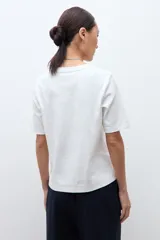 Remera de algodón color blanco, con cuello redondo, mangas cortas y diseño con costuras verticales decorativas en el frente.
