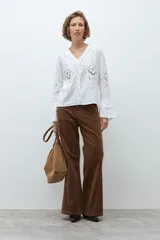 Blusa blanca de manga larga con diseño calado y bordado floral. Presenta un escote en V con detalle de volados frontales y mangas acampanadas con terminación en volado.