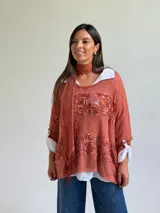 Sweater de punto color naranja con diseño holgado, que incorpora franjas horizontales de encaje con motivos florales. Presenta mangas tres cuartos con puños abotonados y se complementa con una bufanda del mismo tejido y color.
