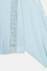 Blusa de escote en pico con cierre frontal de botones, mangas largas abullonadas con bordados a contraste y detalles de encaje tipo entredós y jaretas en el frente.