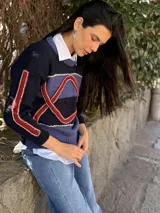 Sweater de tejido de punto con diseño geométrico en tonos azul marino, azul y detalles en rojo. Presenta cuello redondo y mangas largas con bordados lineales.