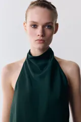 Top de cuello halter color verde oscuro, con escote drapeado, manga sisa y bajo asimétrico. Cierre en la espalda.