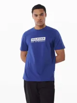 Remera de manga corta Tommy Hilfiger de cuello redondo, confeccionada en puro algodón. Presenta un diseño liso en color azul con un logo gráfico estampado en el pecho enmarcado en un recuadro blanco.