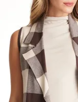 Chaleco tejido largo de la marca Absolutely Famous, con estampado a cuadros en tonos marrón, beige y blanco. Presenta cuello con solapa, abertura central, bolsillos aplicados en la parte delantera, pasadores en la cintura con lazo de ajuste y un tajo central en el ruedo trasero.