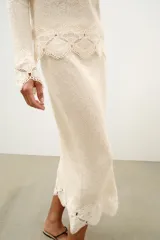 Top de tejido rústico color beige con cuello redondo y mangas largas, con aplicación de crochet a tono en los puños y el ruedo.
