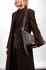 Bandolera Aliada de cuero gris oscuro, con diseño descontracturado, cierre metálico, bolsillo interior y correa ancha regulable con hebilla y argollas metálicas.
