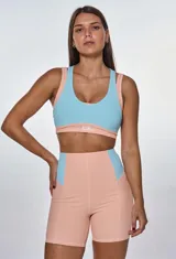 Conjunto deportivo de dos piezas compuesto por un top y un short de tiro alto. El top presenta un diseño de bloques de color en salmón y celeste con escote redondo y espalda deportiva. El short es de corte ajustado, con paneles laterales en contraste de color y textura acanalada.
