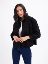 Chaqueta de gamuza sintética color negro, con cuello camisero, bolsillos frontales con solapa, cierre de botones y mangas largas.
