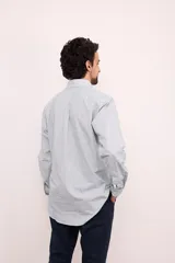 Camisa de corte clásico confeccionada en algodón, con diseño de rayas verticales en tonos claros, cuello abotonado y manga larga. Presenta un pequeño bordado en el pecho.
