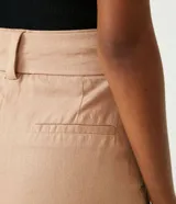 Short de lino y viscosa color tostado, de tiro alto con pliegues delanteros, bolsillos laterales y cinturón incorporado con hebilla cuadrada forrada.