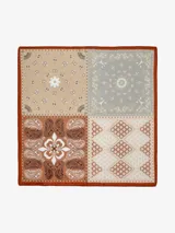 Pañuelo cuadrado con estampado de cuatro paneles, cada uno con un diseño diferente: motivos florales, paisley y geométricos, en tonos beige, gris, marrón y blanco, con borde naranja.