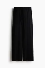 Pantalón de pijama de punto pointelle suave, de color negro, con piernas levemente acampanadas, cintura elástica con ribete de volados y cordón de ajuste.