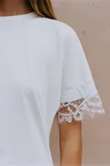 Camiseta negra de algodón con cuello redondo, manga corta y detalle de aplicación de encaje a tono en los puños. Presenta un diseño con bajo asimétrico y frunce lateral.
