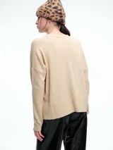 Sweater de tejido de punto color beige, con cuello redondo, hombros caídos y costura central vertical en el frente. Presenta un diseño de corte relajado, con largo asimétrico y aberturas laterales en el ruedo.