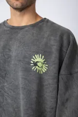 Buzo de cuello redondo y corte oversize, confeccionado en tela friza con efecto de teñido artesanal desgastado. Presenta un estampado pequeño en color verde lima en el pecho y una etiqueta pequeña en el puño.