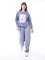 Remera de manga larga color azul, con cuello redondo y un estampado central de flores en tonos pastel sobre un recuadro gris claro.