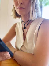 Gargantilla con cordón negro y dije metálico plateado en forma de estribo.