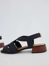 Sandalia de diseño minimalista con tiras anchas de neopreno negro, taco bajo de madera y detalle de tira trasera en color suela.