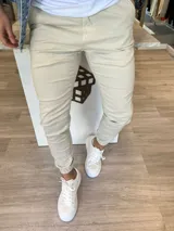 Pantalón chino de gabardina color beige, con corte ajustado, bolsillos laterales y terminación de puños elásticos en los tobillos.