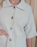 Cardigan de punto color arena, con cuello camisero, cierre frontal de botones y mangas cortas con terminación acanalada. Presenta dos bolsillos frontales tipo parche.