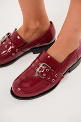 Mocasines color rojo charol con hebilla metálica y ojalillos.