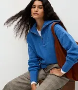 Suéter de punto azul con cuello alto y cierre frontal de cremallera metálica. Presenta textura de líneas verticales, corte regular, mangas largas y terminaciones acanaladas.