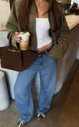 Chaqueta tipo bomber de gamuza en color verde oliva, con cuello camisero, cierre frontal oculto y diseño de corte holgado con hombros caídos.