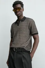 Polo de manga corta con cuello solapa y cierre frontal de dos botones. Tejido de punto con textura de rombos en tonos negro y beige, con ribetes negros en cuello, mangas y bajo.