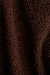 Campera oversized de sherpa suave color marrón oscuro, con cuello elevado, cierre frontal y bolsillos discretos en las costuras laterales. Presenta hombros caídos y mangas largas amplias.