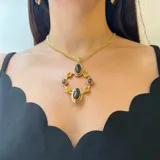 Collar con cadena de eslabones dorados y dije colgante de diseño geométrico en bronce. El dije presenta dos óvalos centrales de nácar y está rodeado por ocho cuentas pequeñas de perla o piedra blanca, engastadas en aros de bronce.