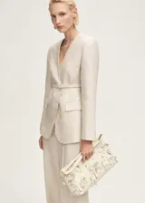 Blazer de lino color beige con diseño cruzado, cuello de pico y hombros estructurados. Incluye un cinturón ajustable con hebilla del mismo tejido y dos bolsillos laterales con solapa.