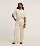 Pantalón largo de cintura alta color beige, confeccionado en tejido viscolino, con trabillas en la cintura, cinturón de cuerda para lazo, cierre tradicional y pliegues.