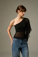 Top asimétrico de un solo hombro, color negro, con diseño ajustado al cuerpo y sección central y manga de tela transparente.