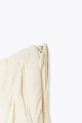 Falda midi color crudo, de tiro medio y confeccionada en viscosa. Presenta detalle de pliegues y bajo asimétrico. Cierre lateral con cremallera oculta.