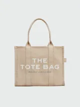 Bolso tipo tote de gran tamaño en color beige, confeccionado en lona resistente. Presenta el logo distintivo de la marca estampado en la parte frontal con letras blancas. Cuenta con doble asa superior para llevar al hombro y cierre superior con cremallera.