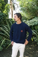 Sweater de tejido de punto en color azul marino, con cuello redondo y mangas raglán. Presenta un bordado distintivo en color naranja en el pecho.