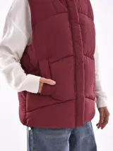 Chaleco acolchado negro con capucha y cierre frontal de cremallera y broches.